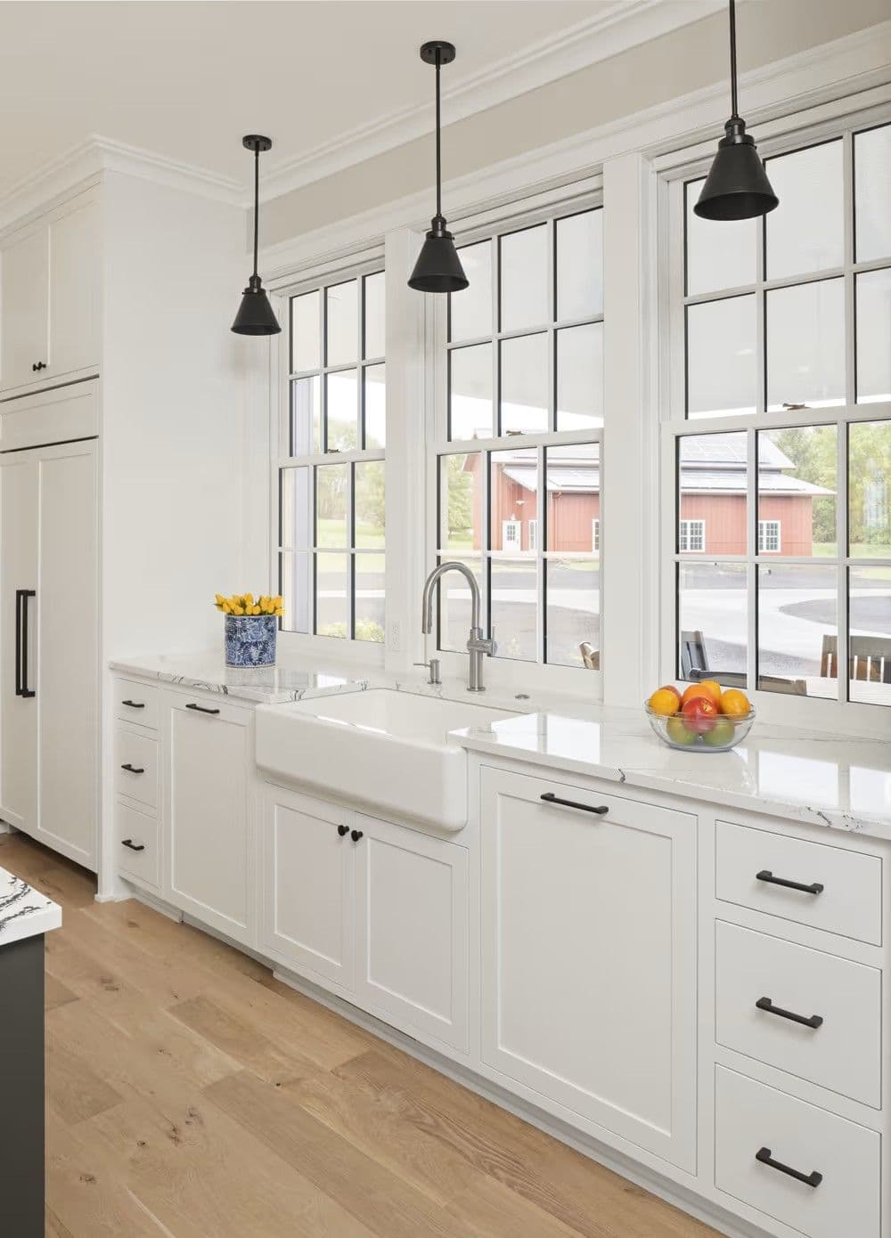 Kitchen with white cabinets and farmhouse sink in front of three white Marvin ultimate double hung windows.