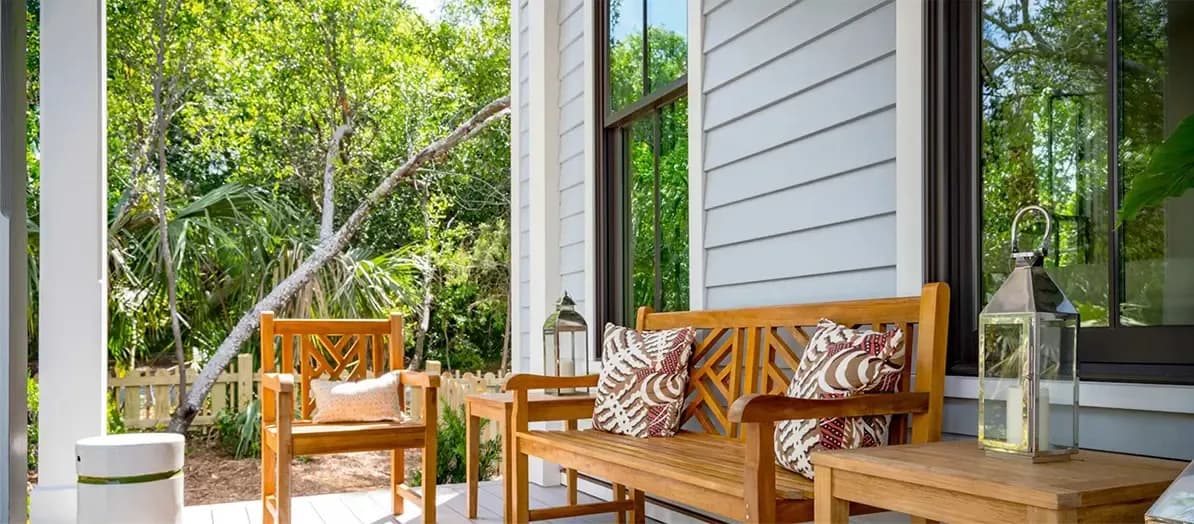 Outdoor furniture sits on the porch of a gray house with new siding.