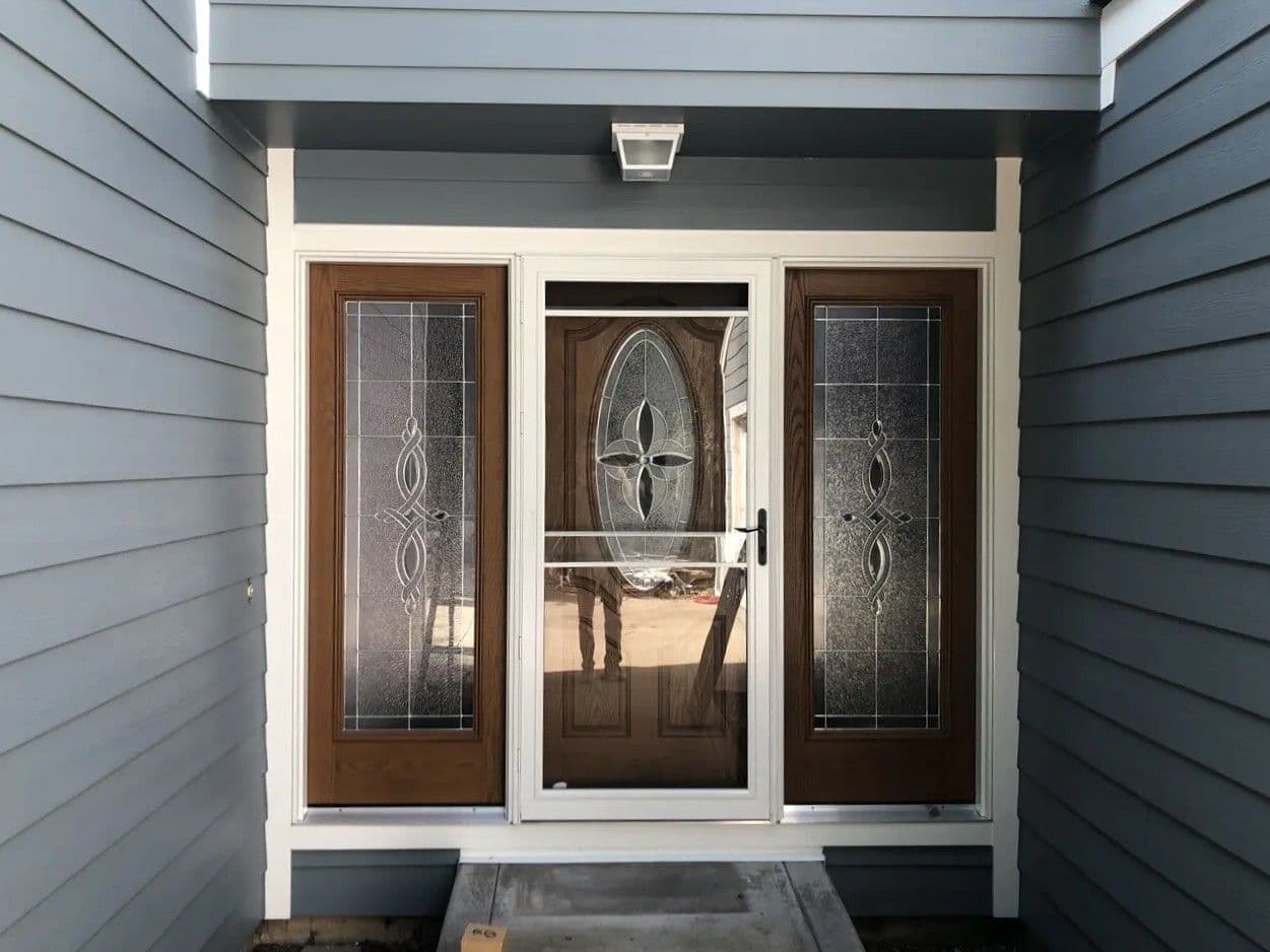 Newly-replaced entry door with textured windows on either side and a white storm door.